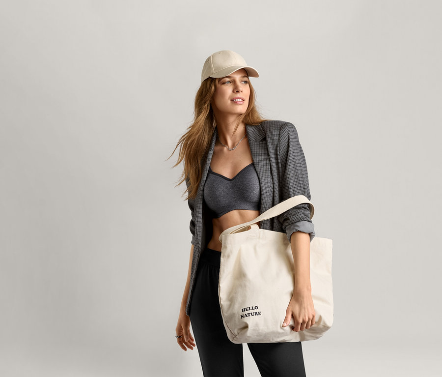 Frau trägt einen Sport-BH, einen Blazer und eine Mütze und hält eine Tragetasche.