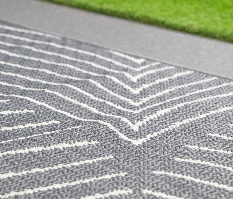 Nahaufnahme eines grau-weiß gestreiften Teppichs neben einem Rasenstück.