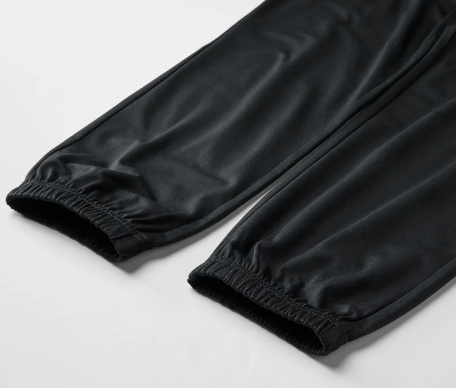 Nahaufnahme von zwei schwarzen Hosenbeinen mit elastischen Bündchen auf einem weißen Hintergrund.
