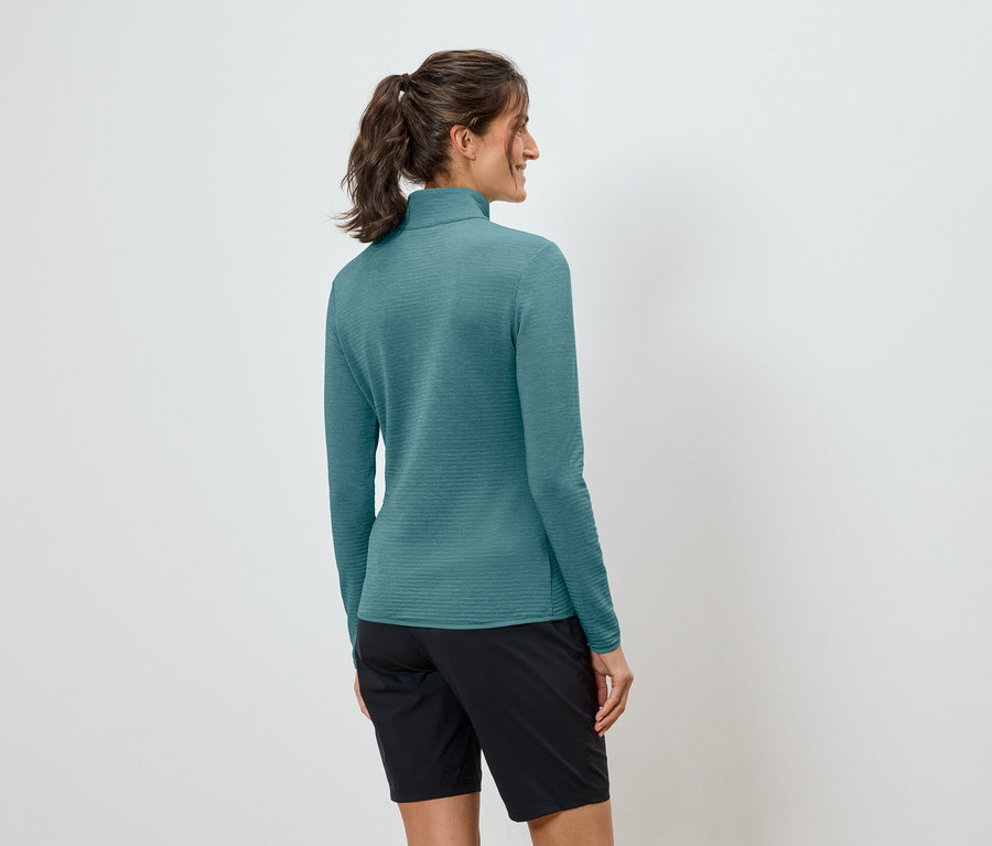 Eine Frau mit Pferdeschwanz trägt ein türkisfarbenes, langärmeliges Oberteil und schwarze Shorts.