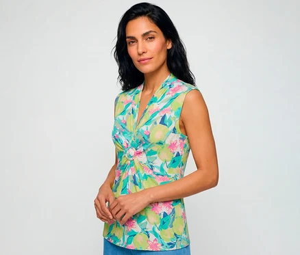 Frau trägt ein ärmelloses Olsen Shirt mit farbenfrohem grünem, pinkem und türkisfarbenem Obst- und Blumenmuster, V-Ausschnitt und dekorativem Ringdetail vorne.