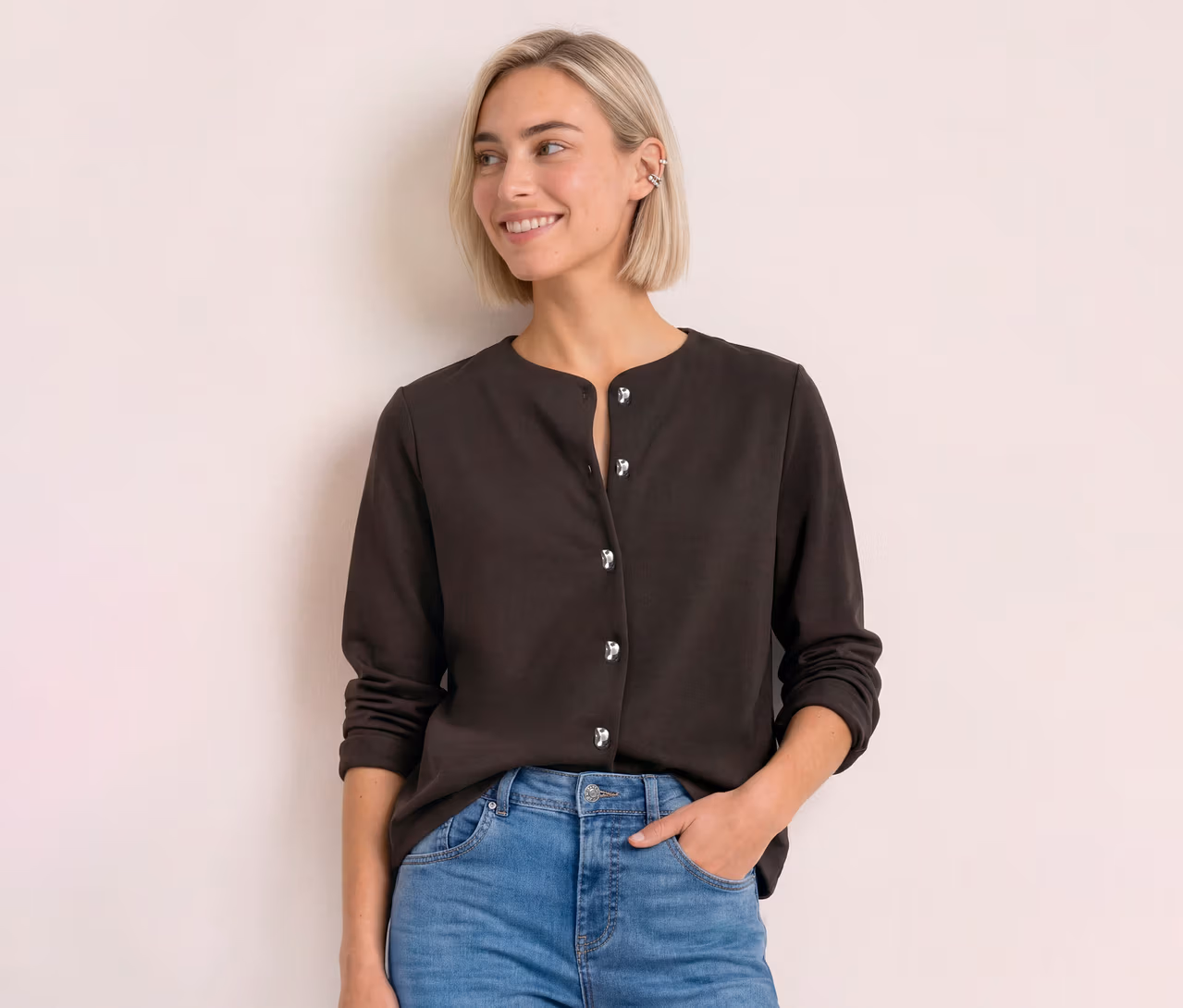 Junge Frau mit blondem Bob trägt einen dunkelbraunen Street One Cardigan mit silbernen Knöpfen und Jeans, lächelt zur Seite.
