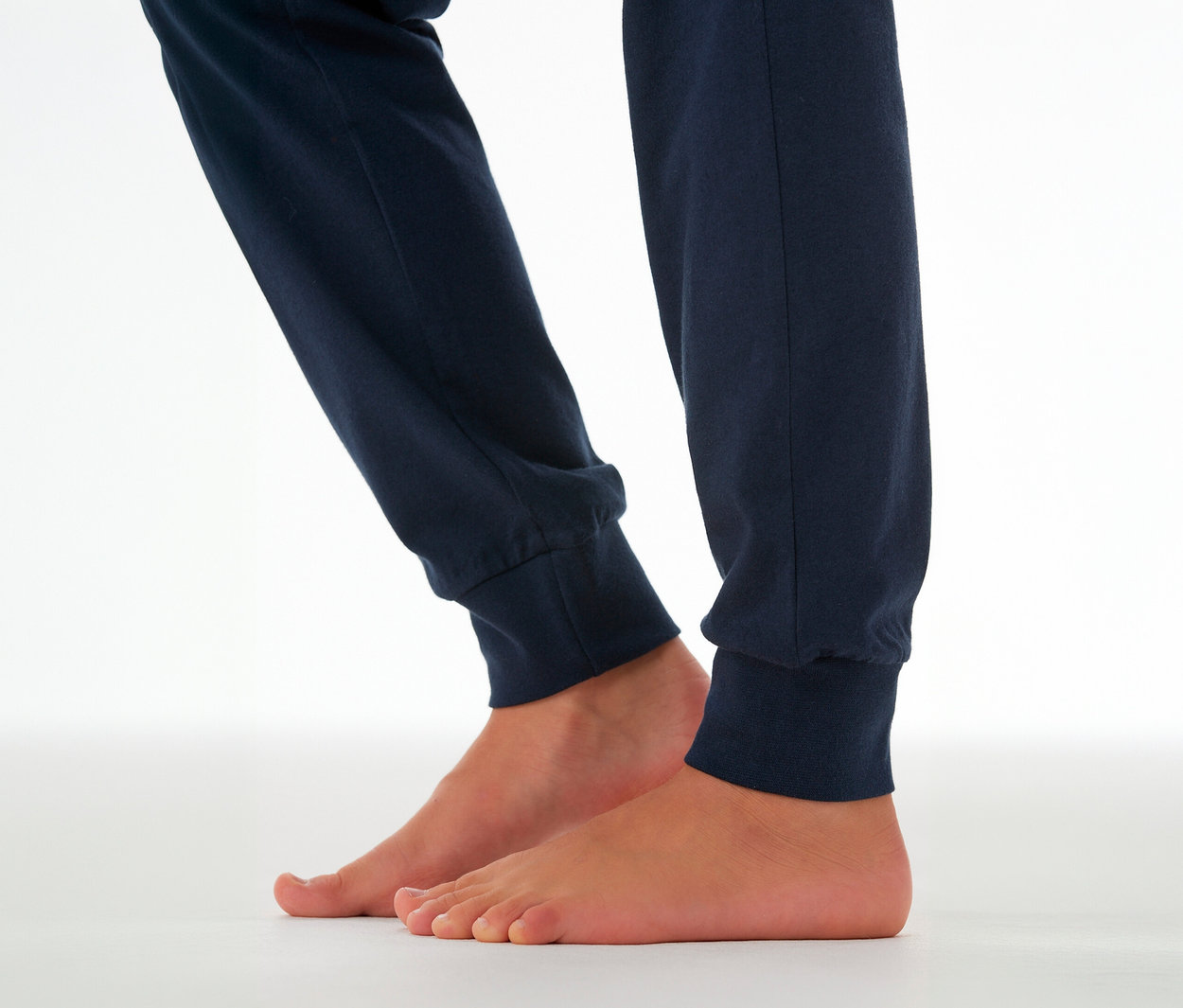 Kinderbeine in dunkelblauer SCHIESSER Kinder-Pyjamahose mit Bündchen, die Füße sind barfuß.