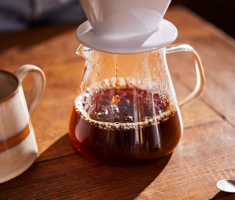 Kaffee läuft in eine Kaffeekanne aus Glas, daneben steht eine Tasse.