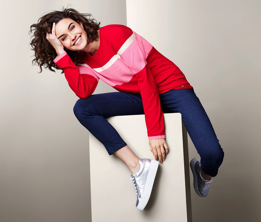 Frau sitzt auf einem Würfel und trägt einen Feinstrickpullover im Colorblocking-Dessin.