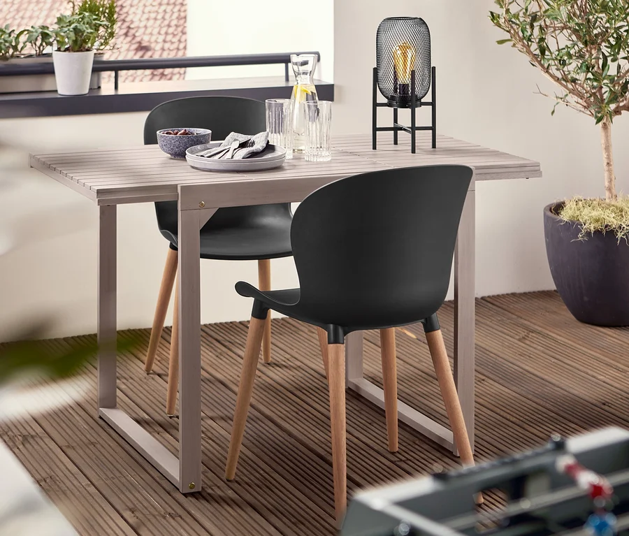 Zwei schwarze Schalenstühle aus recyceltem Kunststoff stehen an einem Ausziehtisch »Leira« neben einer LED-Outdoor-Tischleuchte.