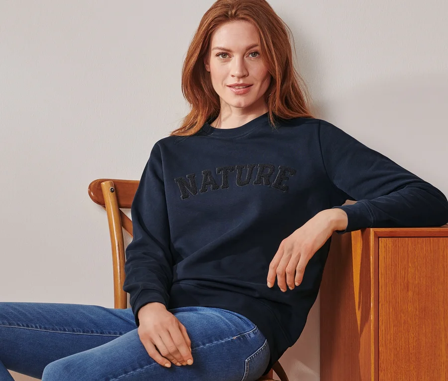 Frau sitzt auf einem Stuhl und trägt ein Sweatshirt mit Wording.