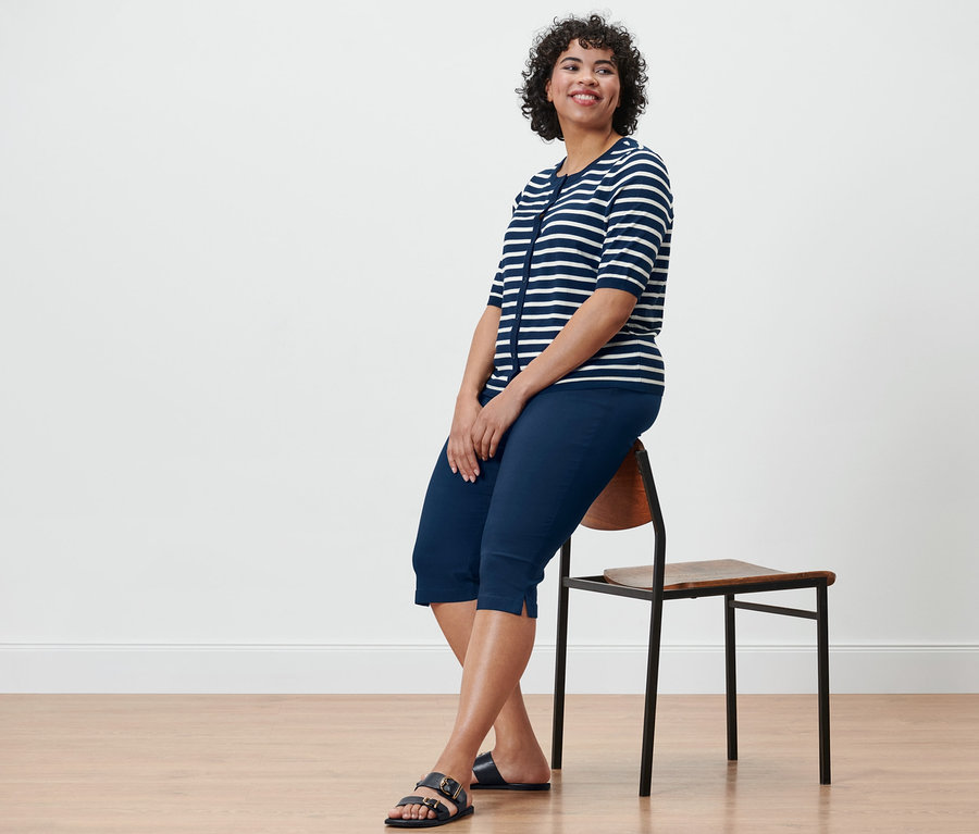 Eine Frau sitzt auf einem Stuhl und trägt einen blauen Feinstrick-Cardigan und eine marineblaue Bengalin-Hose in 3/4-Länge.