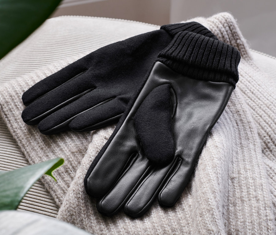Schwarze Lederhandschuhe liegen auf einem Pullover.