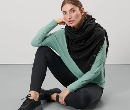 Eine Frau sitzt auf dem Boden und trägt einen schwarzen 3-in-1-Oversize-Schal.