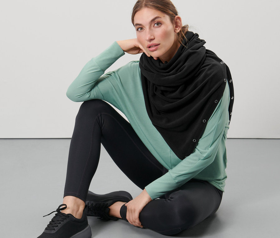 Eine Frau sitzt auf dem Boden und trägt einen schwarzen 3-in-1-Oversize-Schal.