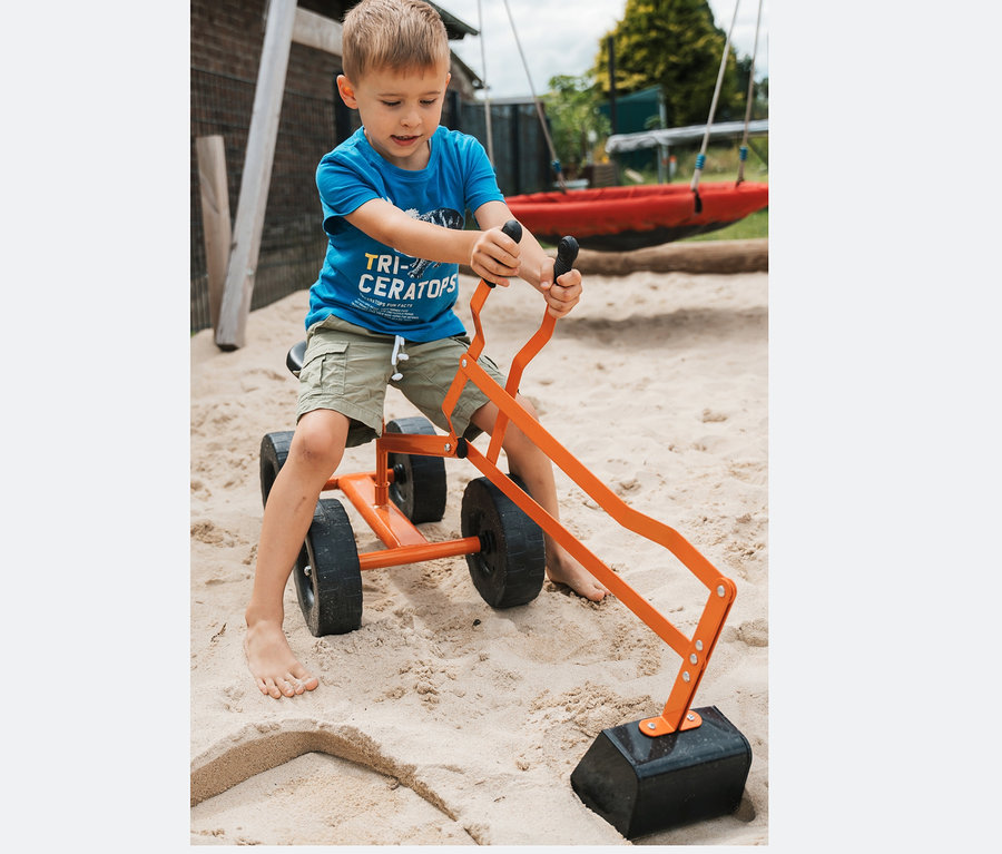 Ein Junge spielt mit einem small foot Bagger mit Rädern im Sandkasten.