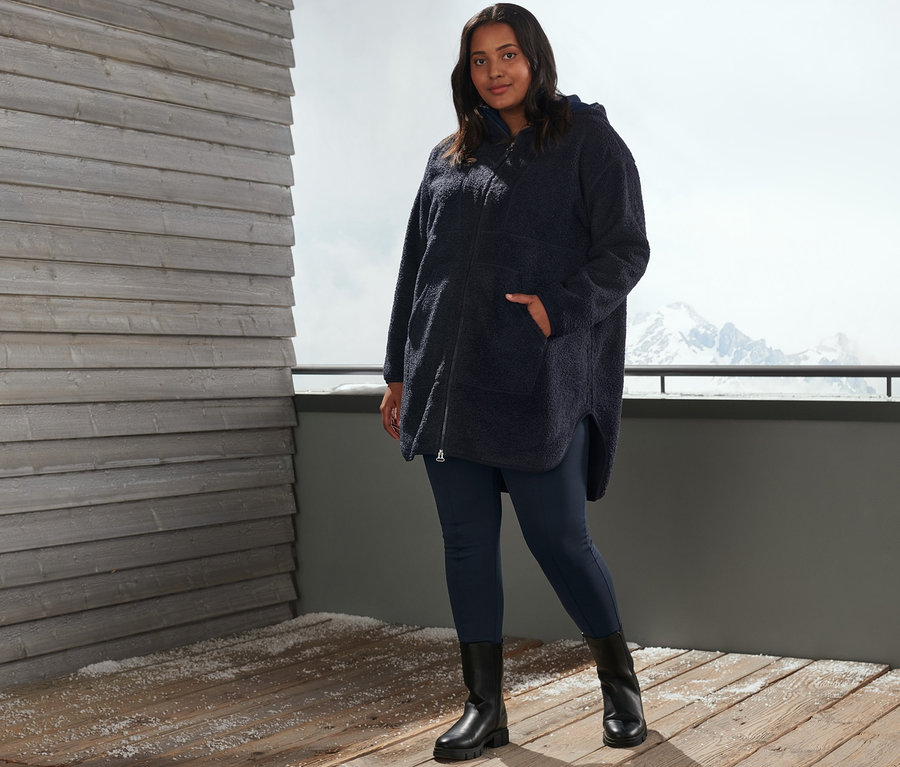 Frau posiert draußen in blauen Thermotights und einem Oversized Teddymantel.
