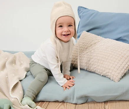 Lächelndes Baby sitzt und trägt eine Baby-Strickmütze-und-Strickschal.