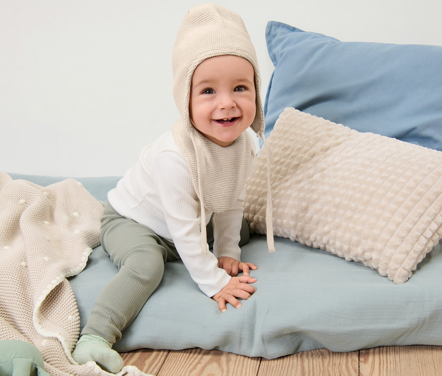 Lächelndes Baby sitzt und trägt eine Baby-Strickmütze-und-Strickschal.