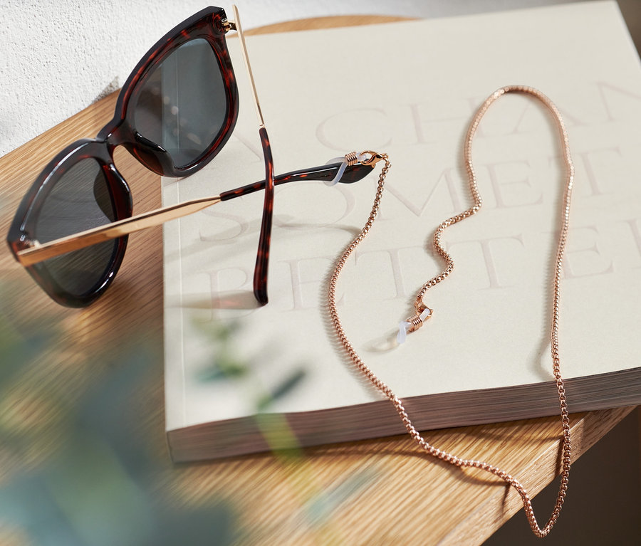 Sonnenbrille und Brillenkette liegen auf einem Buch auf einem Holztisch.