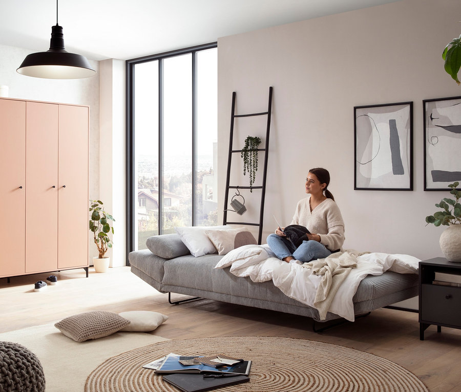 Eine Frau sitzt auf einem grauen DOMO collection Daybed »Molde Leif55« und hält etwas in ihren Händen.