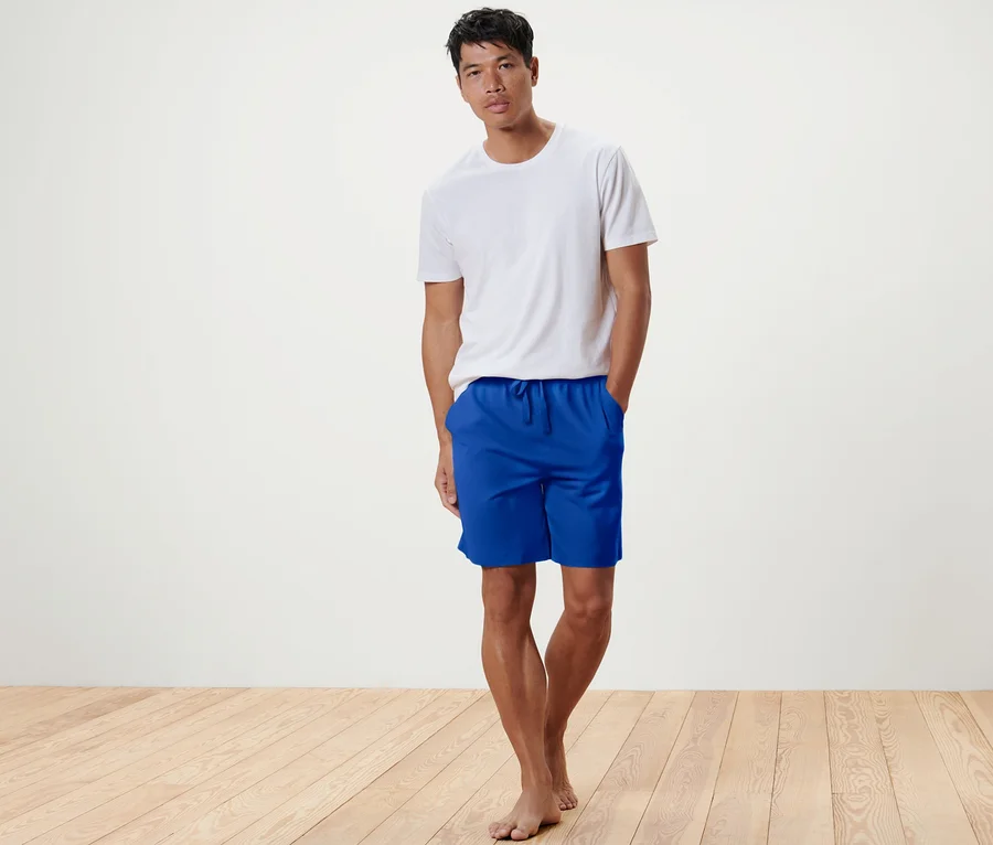 Mann steht in weißem T-Shirt und blauen Relaxshorts.