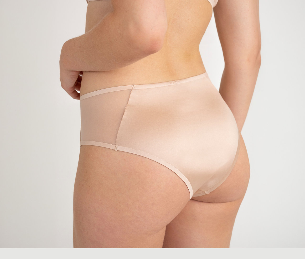 Eine Frau von hinten trägt einen Passionata High Waist Slip «Bianca» in Dune mit transparenten Seiteneinsätzen.