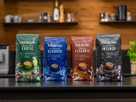 Vier Packungen Eduscho Kaffee verschiedener Sorten stehen auf einem Tisch vor einer Küchenzeile.
