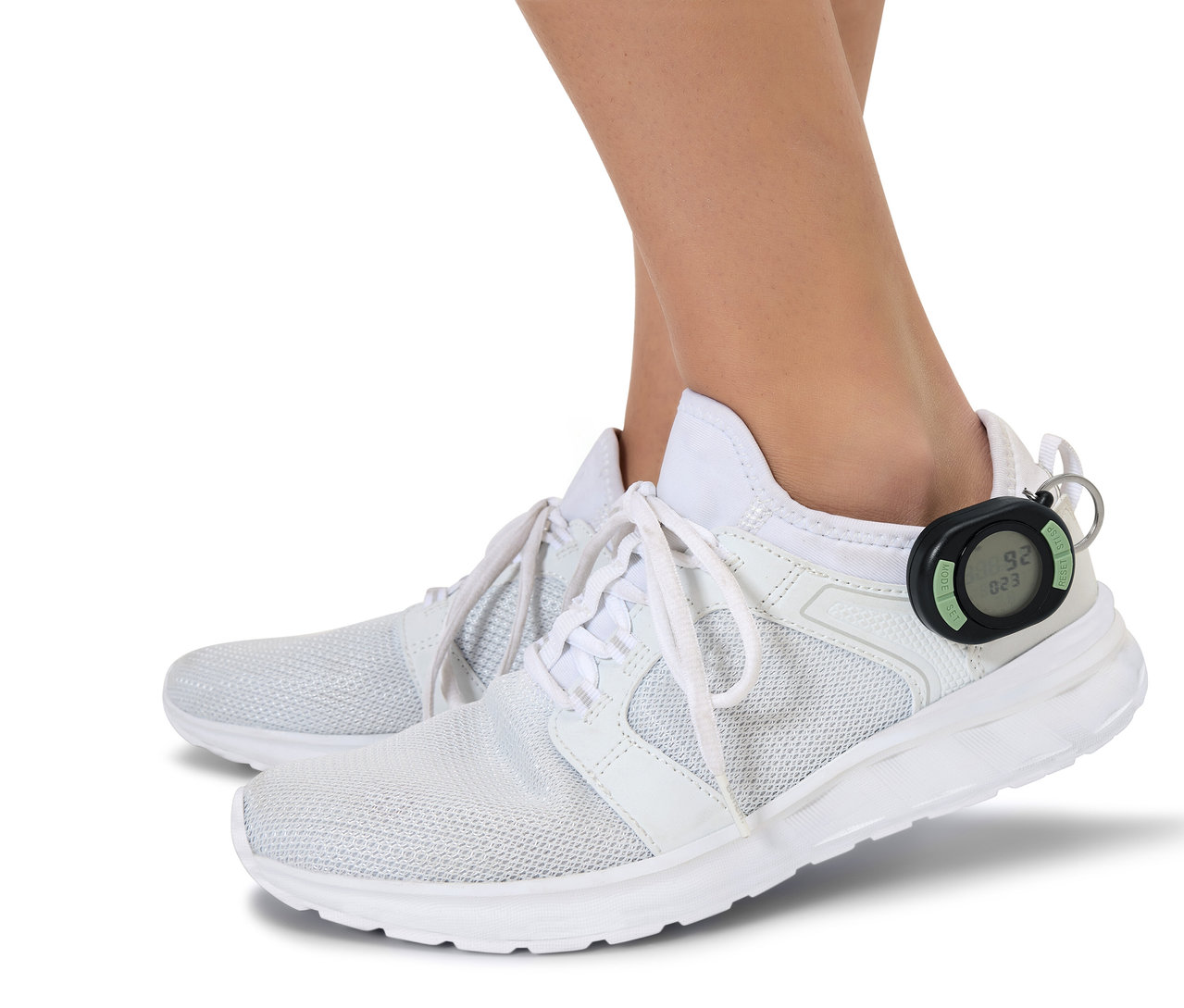 Füße in weißen Schuhen, an der Ferse eines Schuhs ist ein schwarzer Schrittzähler befestigt.