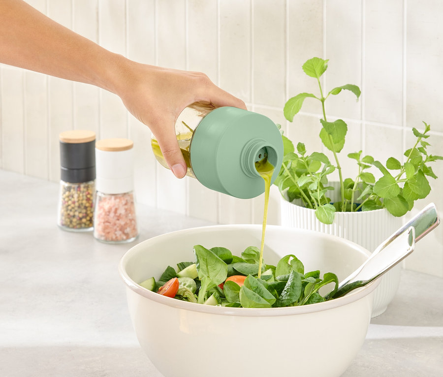 Eine Hand gießt Dressing aus einer Dressingflasche in eine Schüssel Salat.