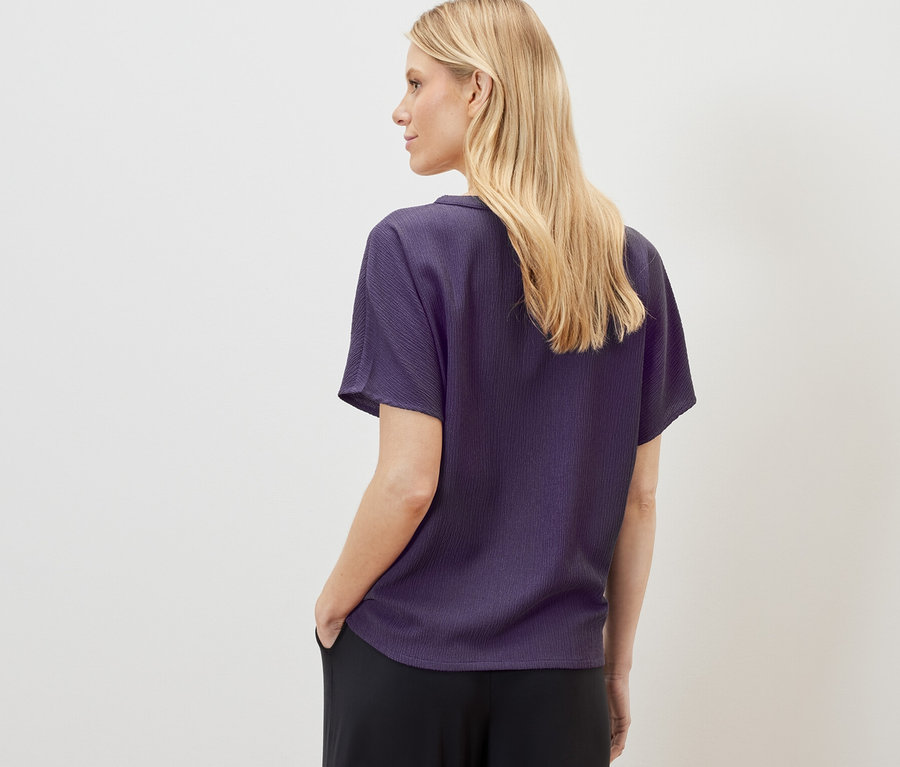 Blonde Frau trägt eine strukturierte Kurzarmbluse und schwarze Hosen.