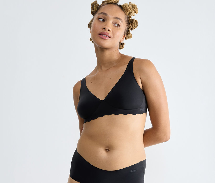 Frau mit kleinen Haarknoten trägt schwarzen sloggi ZERO Microfibre 2.0 Soft bra und passende Unterwäsche.