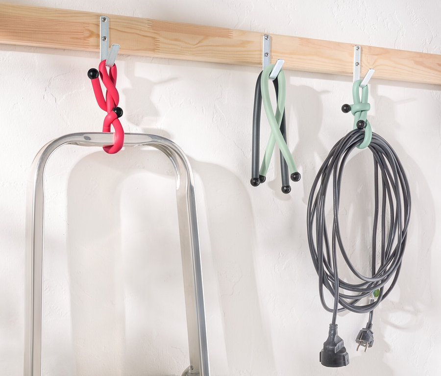 Eine Leiter steht unter einer Holzleiste mit Haken, an denen Power Kabelbinder in Rot, Grün und Schwarz hängen.