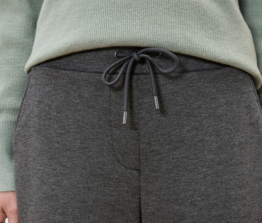 Detailaufnahme einer Frau, die graue Jogginghose und einen mintgrünen Pullover trägt.