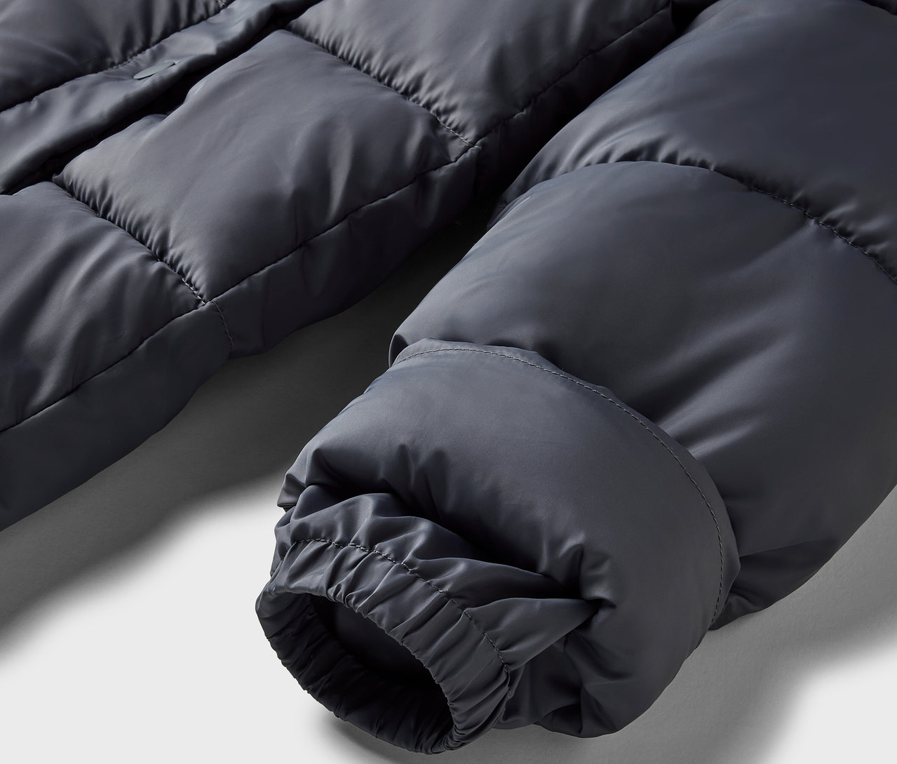 Detailaufnahme einer grauen Daunenjacke mit elastischem Bündchen.