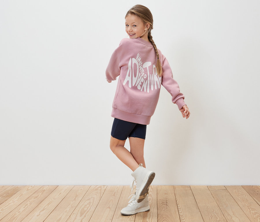 Mädchen blickt über die Schulter, trägt ein rosa Kinder-Sweatshirt.