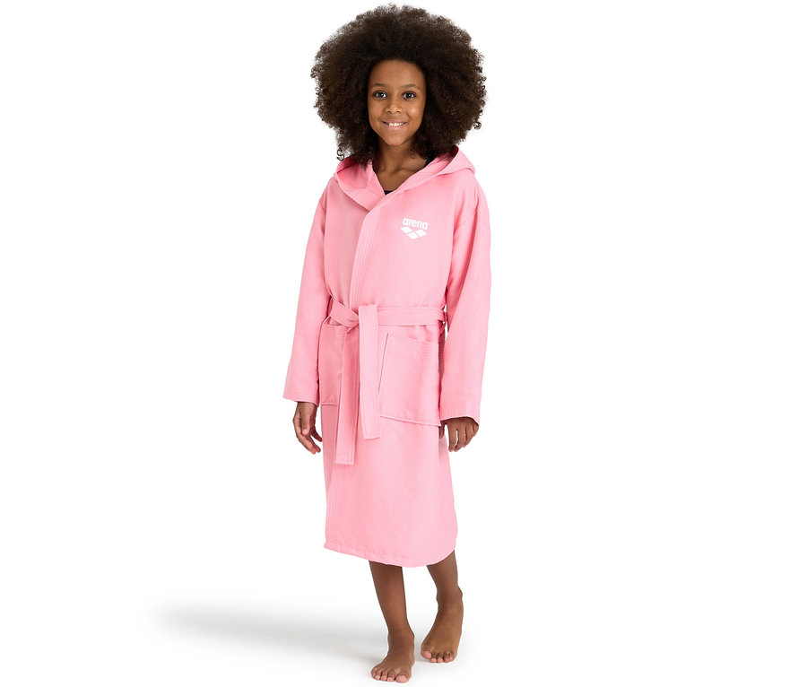 Lächelndes Mädchen mit Lockenhaar trägt einen rosa arena Kinder-Bademantel Zeal Plus JR mit Kapuze, gebunden an der Taille, und steht barfuß.