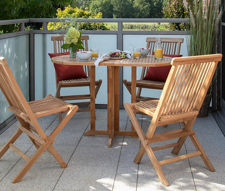 Vier hölzerne Klappstühle umgeben einen runden Tisch mit roten Kissen, Getränken und Snacks auf einem Balkon. Auf dem Tisch steht ein deVries Balkontisch, Teak, 60 x 120.