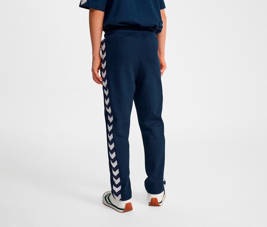 Person von hinten trägt blaue HUMMEL HMLJR Archive Regular Poly Pants mit weißen Winkelstreifen an der Seite.
