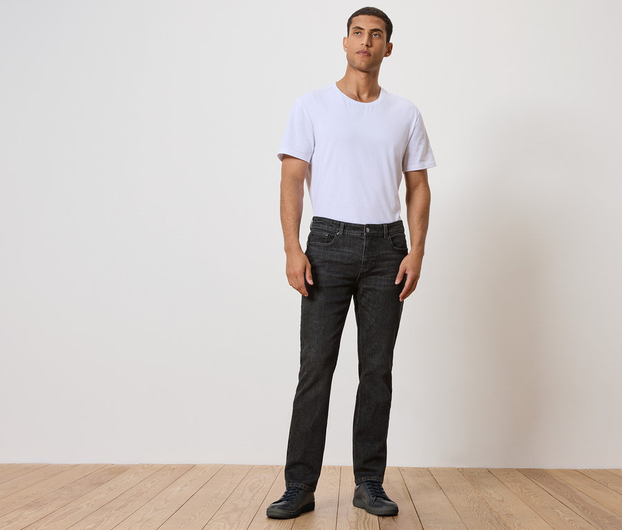 Mann steht auf Holzboden, trägt schwarze Jeans und weißes T-Shirt.