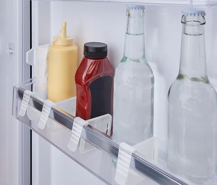Im Kühlschrankregal stehen eine gelbe Senfflasche, eine rote Ketchupflasche und zwei Glasflaschen mit Wasser.
