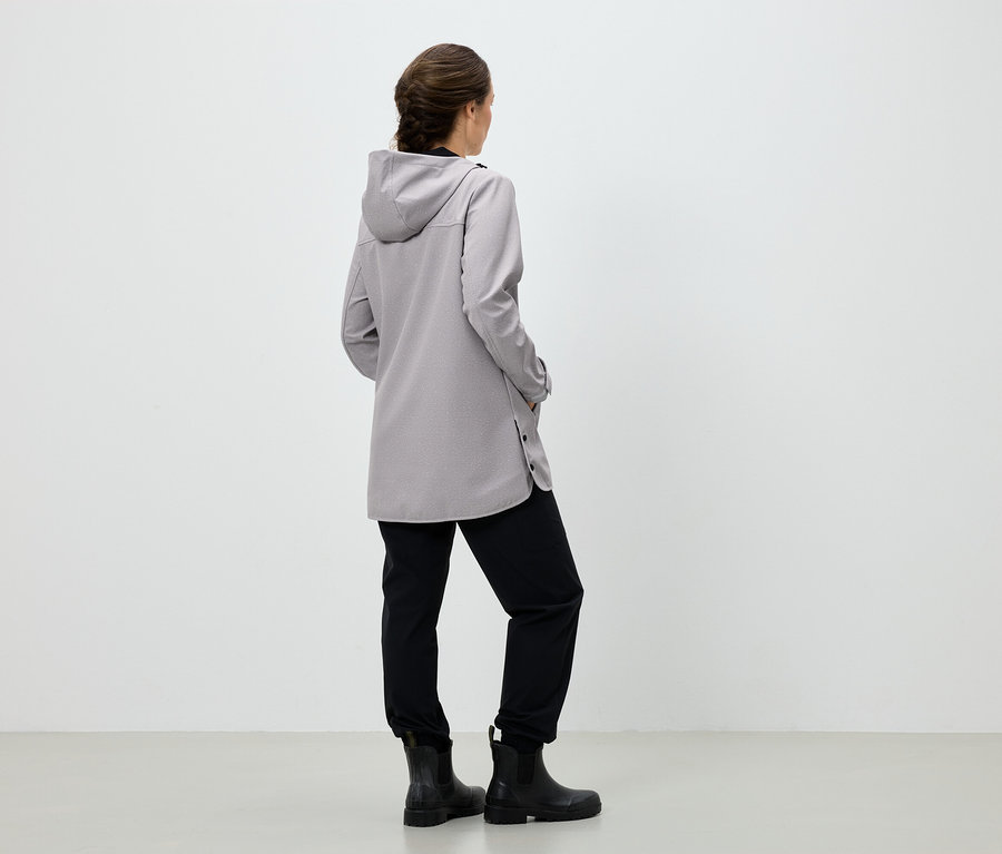 Frau mit dem Rücken zur Kamera trägt einen grauen Mantel mit Kapuze, eine schwarze Hose und schwarze Stiefel.