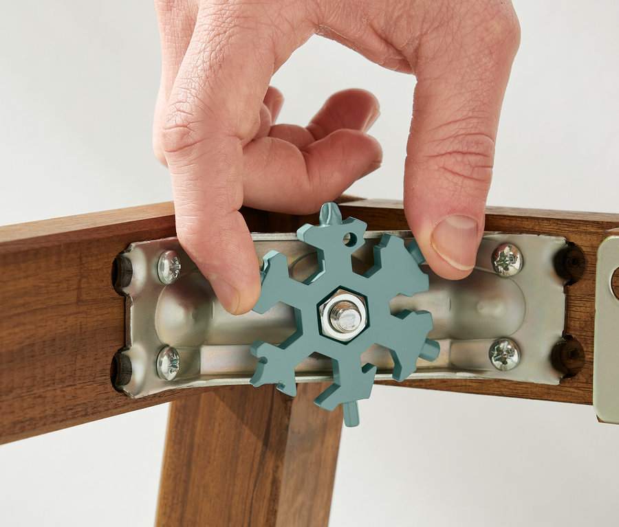 Eine Hand hält einen Multifunktionsschlüssel an einer Schraube an einem Holzrahmen.