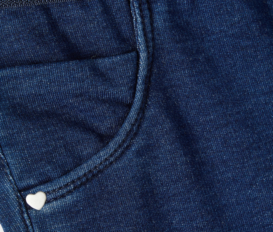 Detailaufnahme einer blauen Jeanshose mit einer kleinen Tasche und einem herzförmigen Knopf.
