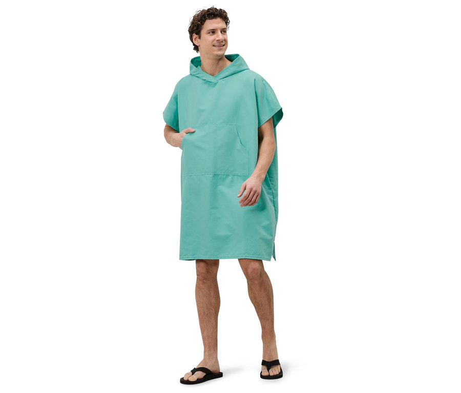 Ein Mann steht in einem türkisfarbenen Badeponcho mit Kapuze und schwarzen Flip-Flops vor einem weißen Hintergrund.