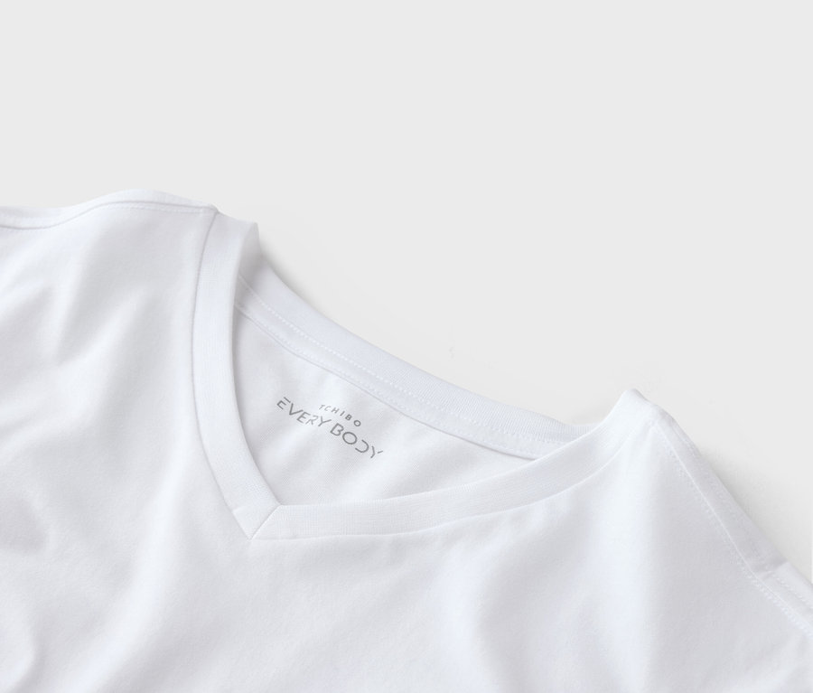 Nahaufnahme eines weißen T-Shirts mit V-Ausschnitt und dem Tchibo Every Body-Logo am Kragen.