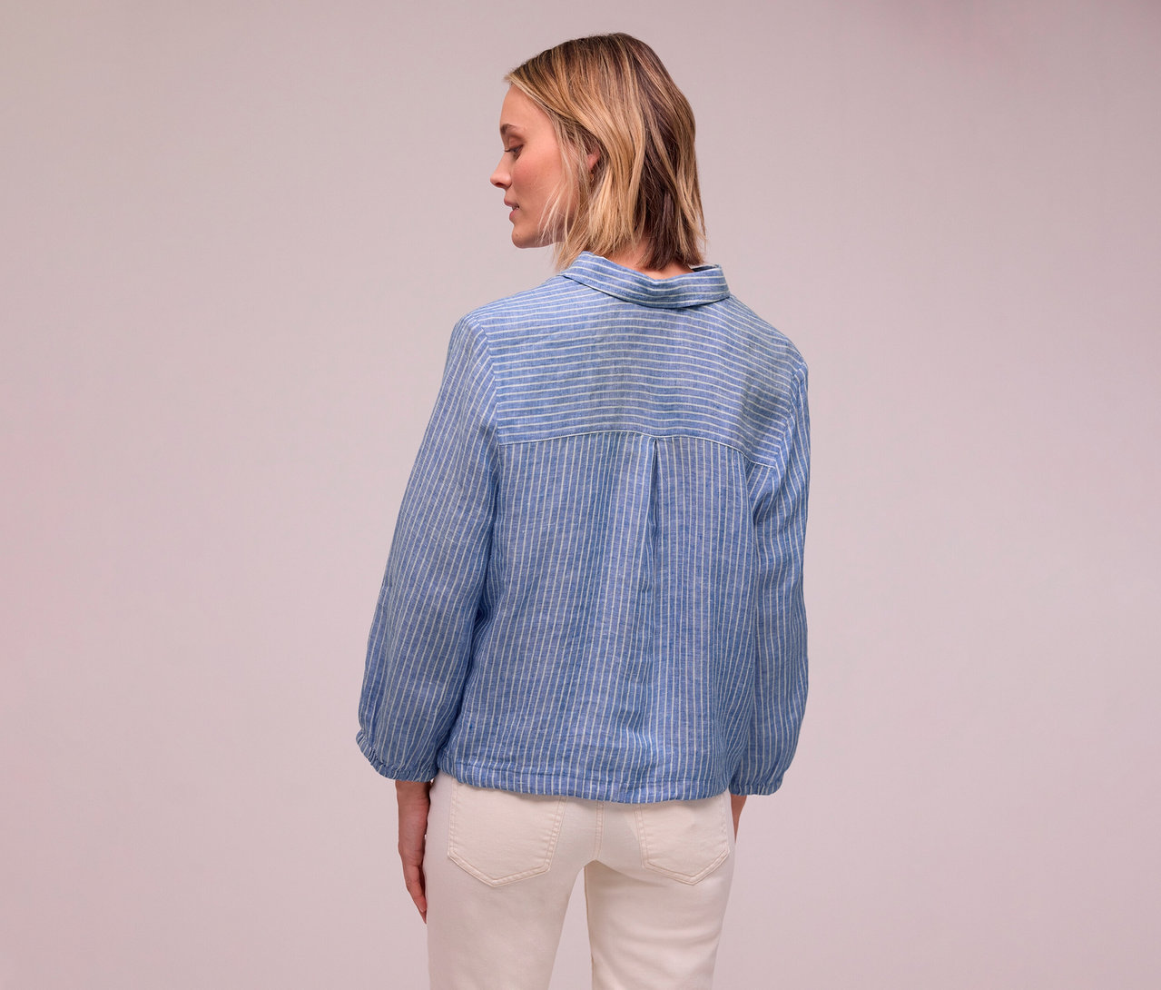 Frau von hinten in blau-weiß gestreifter Bluse und weißen Jeans.