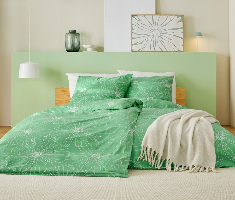 Ein Bett mit grünem Bettbezug mit weißem Blumenmuster, einer weißen Decke und einem hellgrünen Kopfteil.