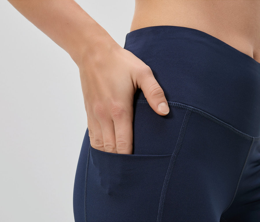 Frau steckt Hand in die Tasche einer marineblauen Leggings.