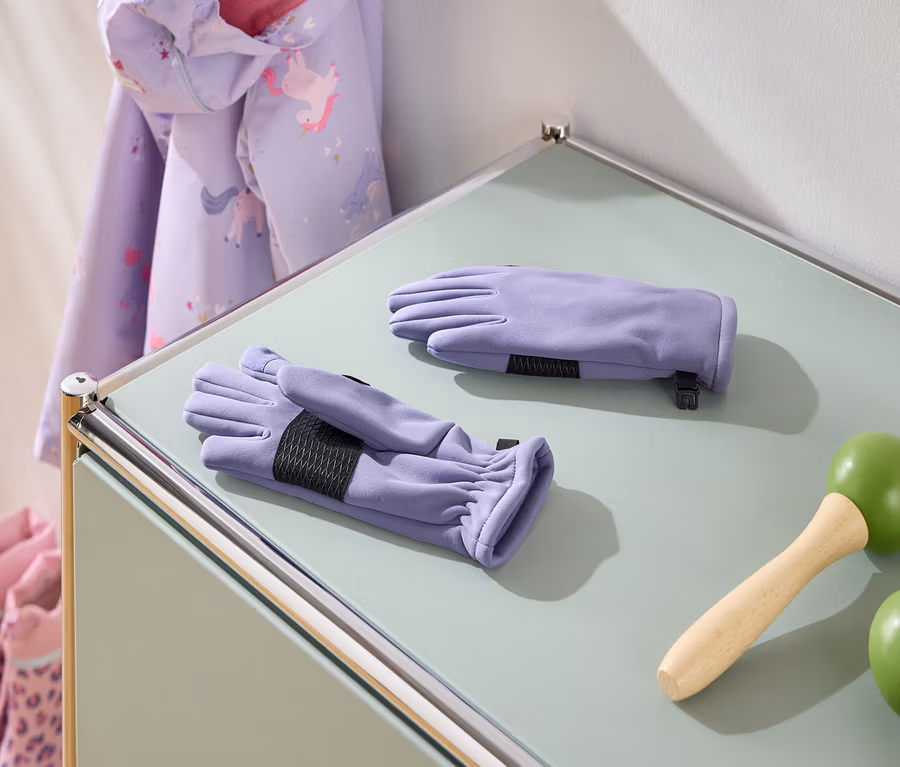 Auf einem Tisch liegen lila Handschuhe, ein Springseil mit grünen Griffen, eine Jacke mit Einhornmuster und rosa Stiefel.