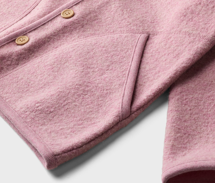 Nahaufnahme einer rosafarbenen Wolljacke mit zwei Knöpfen und einer aufgesetzten Tasche.