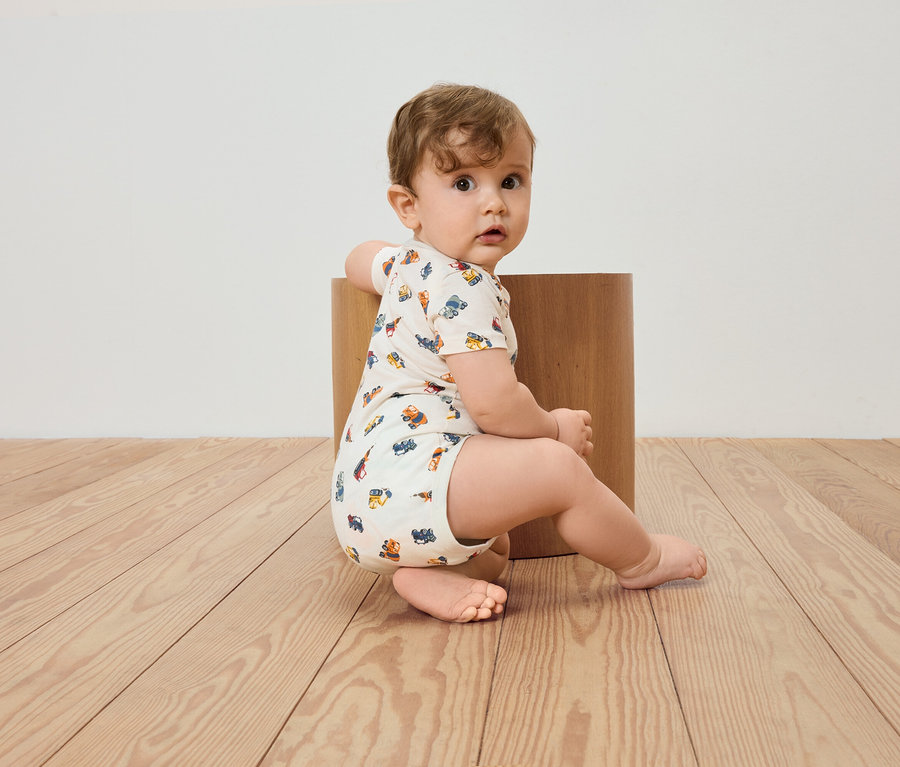 Ein Baby sitzt auf einem Holzboden und lehnt an einem Holzhocker.