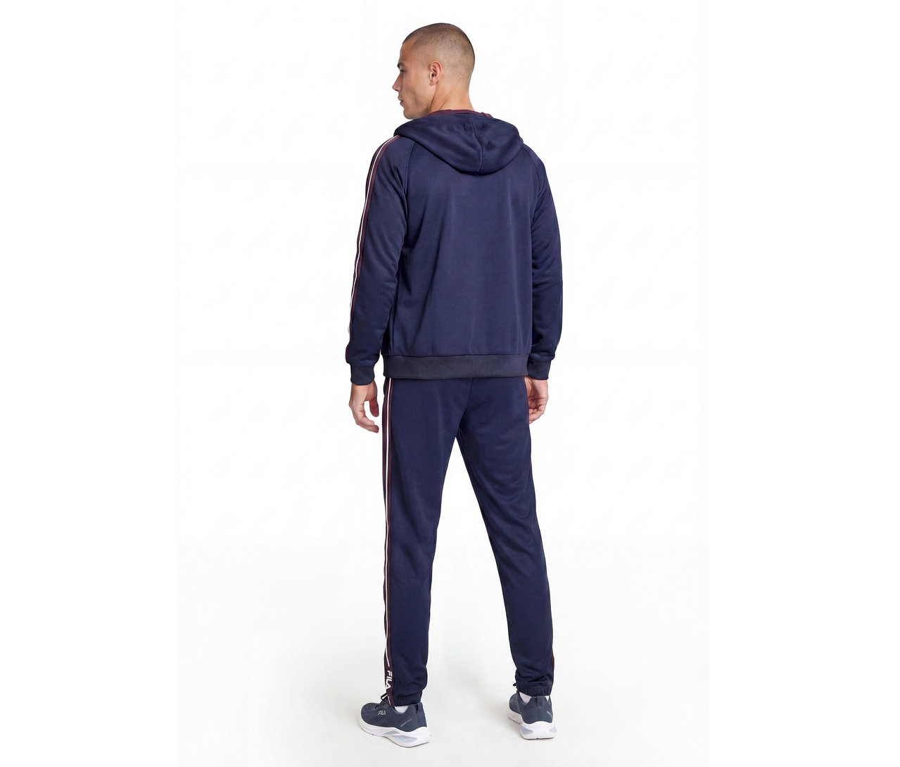 Mann von hinten in einem dunkelblauen Trainingsanzug mit rot-weißen Streifen an Ärmeln und Hosenbeinen sowie dunklen Turnschuhen.