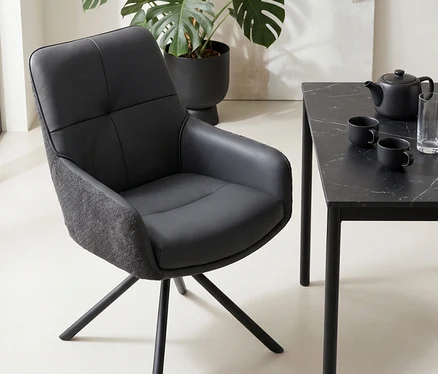 Schwarzer Esszimmerstuhl mit Drehfuß neben einem schwarzen Tisch mit Marmoroptik, Teekanne und Tassen. Im Hintergrund eine große Monstera-Pflanze.